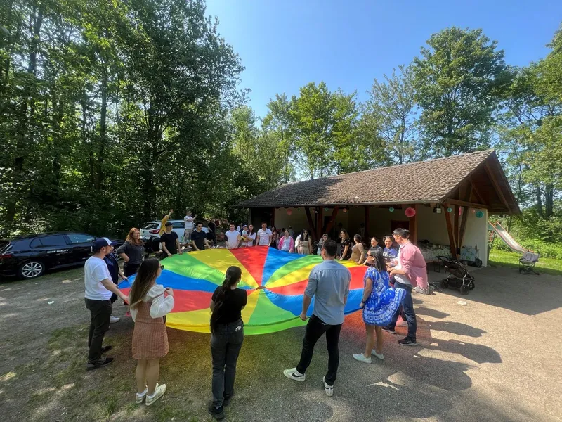 Gruppe spielt mit einem bunten Schwungtuch vor einer Hütte